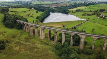 A historic railway viaduct stretching across lush green hills with a reservoir in the background