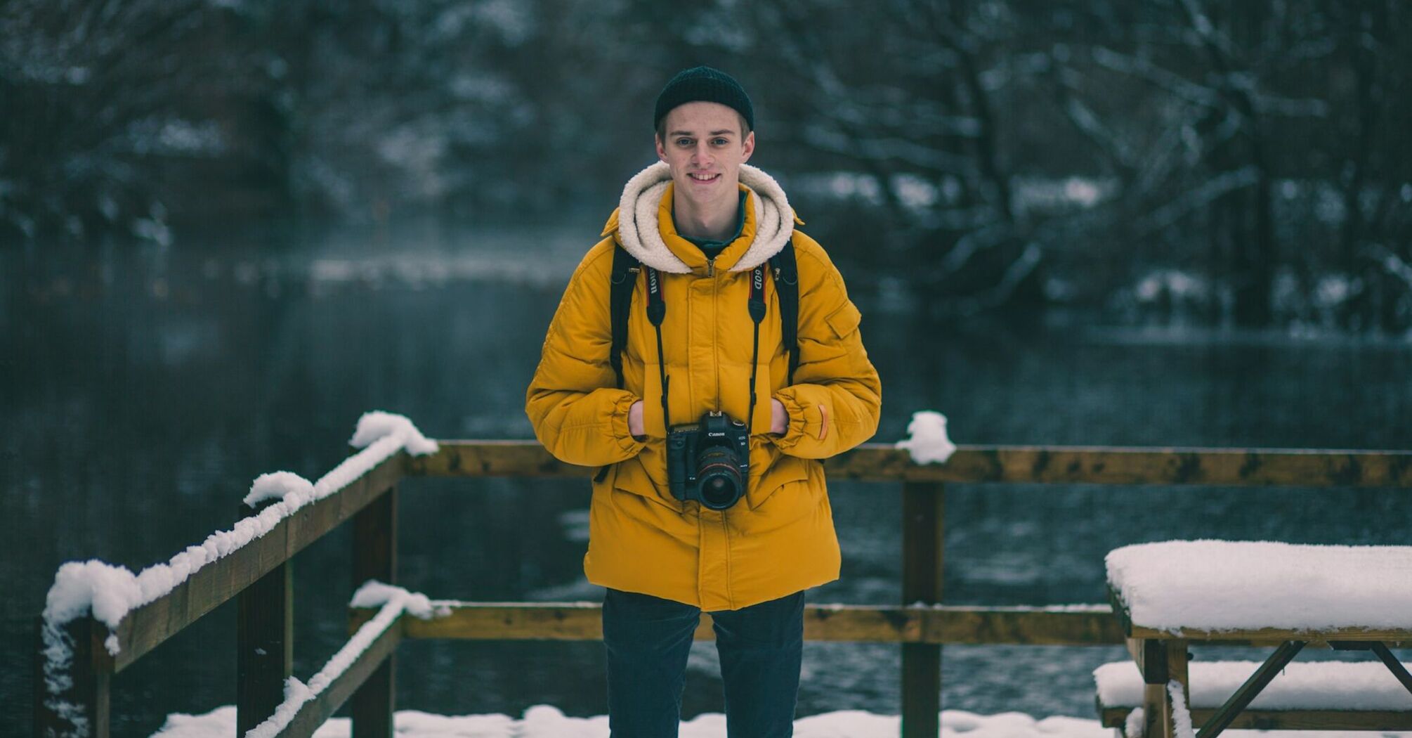 A traveler wearing a yellow jacket with a camera, standing in a snowy winter landscape