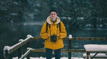 A traveler wearing a yellow jacket with a camera, standing in a snowy winter landscape