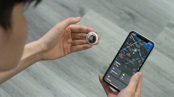 A person holding an Apple AirTag and checking luggage location on a smartphone screen