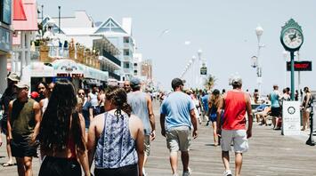 A crowded boardwalk filled with people enjoying a sunny day, with shops and signs in the background