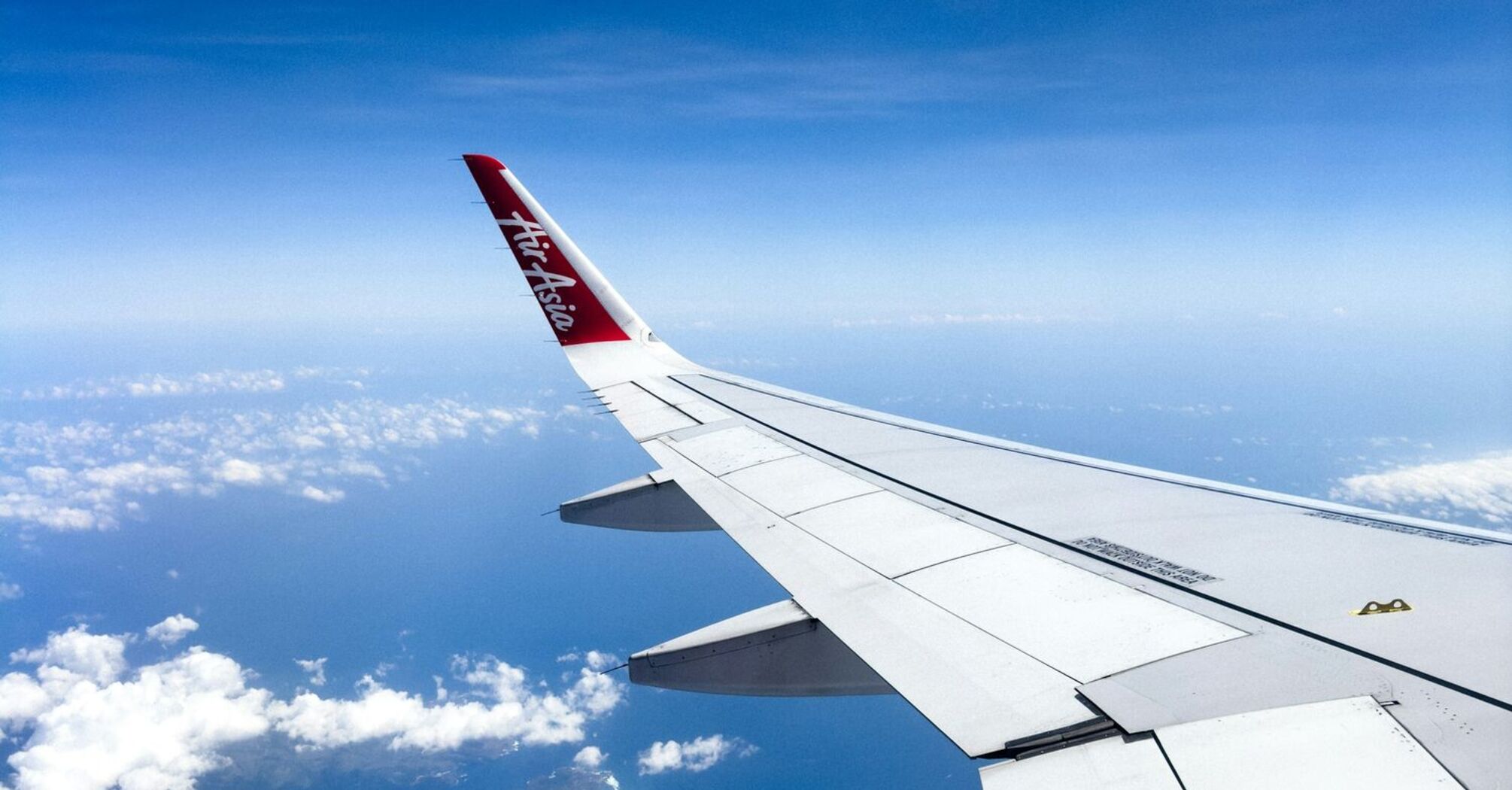 Airplane wing with AirAsia logo flying over islands and ocean under clear blue skies