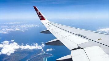Airplane wing with AirAsia logo flying over islands and ocean under clear blue skies