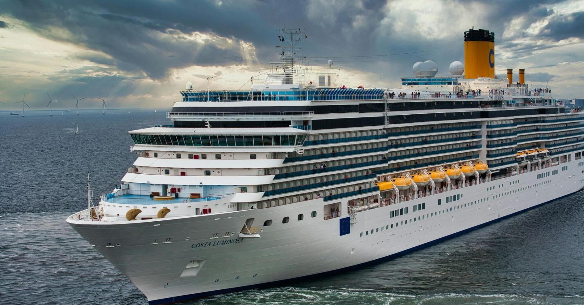 A large modern cruise ship sailing in open waters under a dramatic cloudy sky