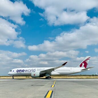A Qatar Airways airplane featuring the oneworld alliance logo on a runway under a clear sky