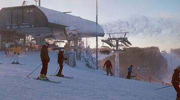 Skiers prepare at the base of a snowy slope near a ski lift station during sunrise