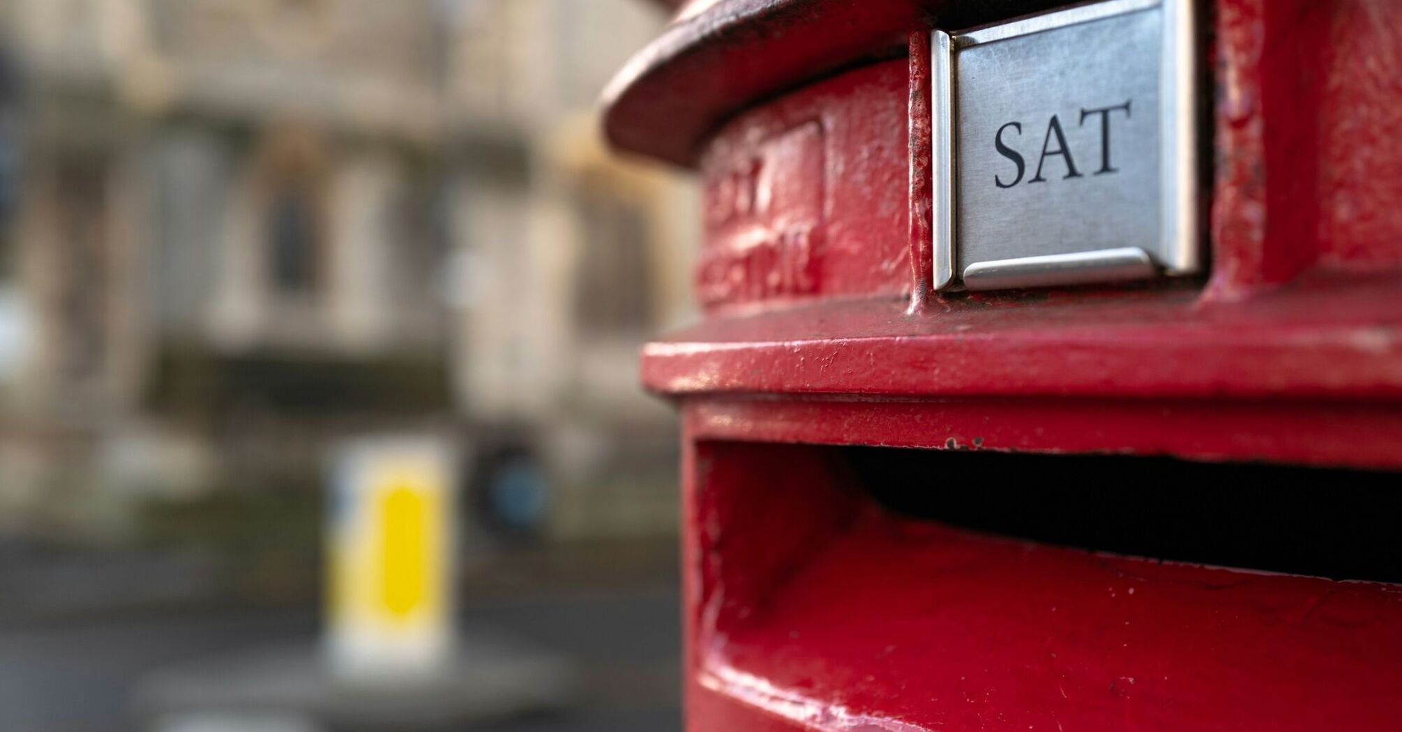 Close-up of a red British postbox with 'SAT' delivery indicator