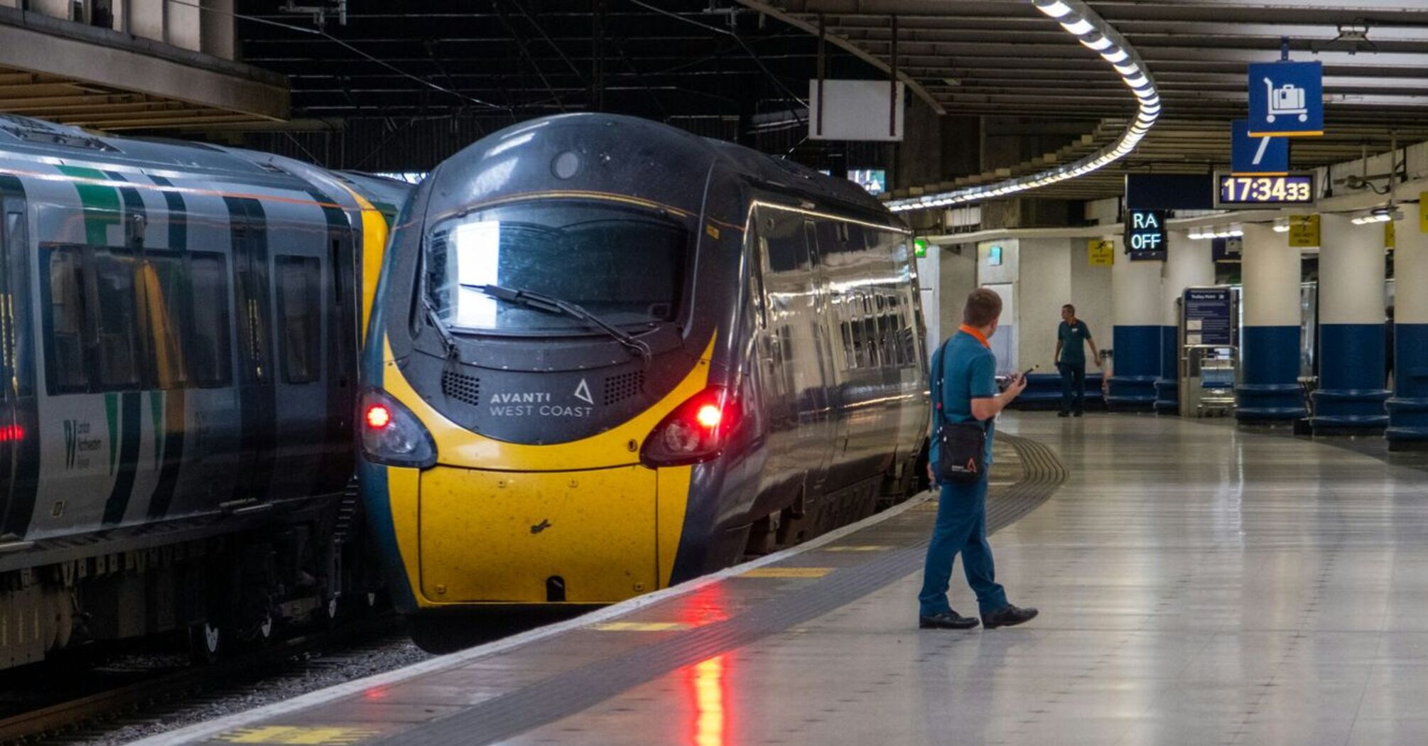 A stationary Avanti West Coast train at a platform in a modern railway station with passengers waiting nearby