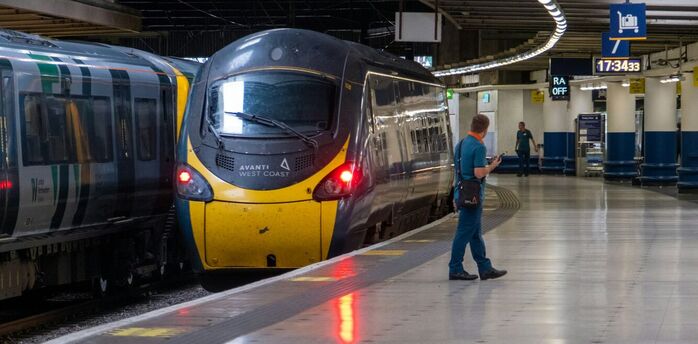 A stationary Avanti West Coast train at a platform in a modern railway station with passengers waiting nearby