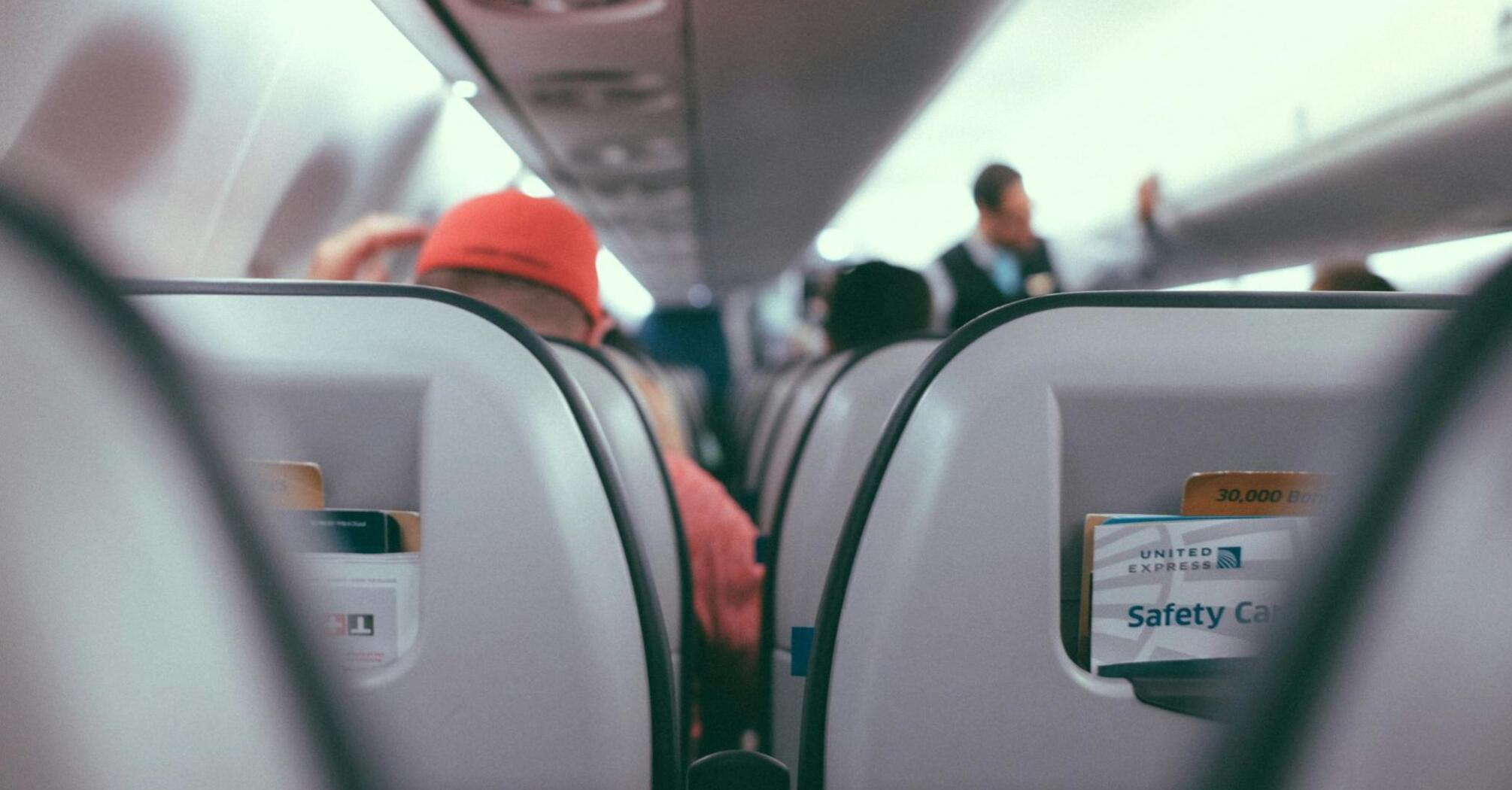 View of an airplane cabin with passengers seated and safety cards in seat pockets