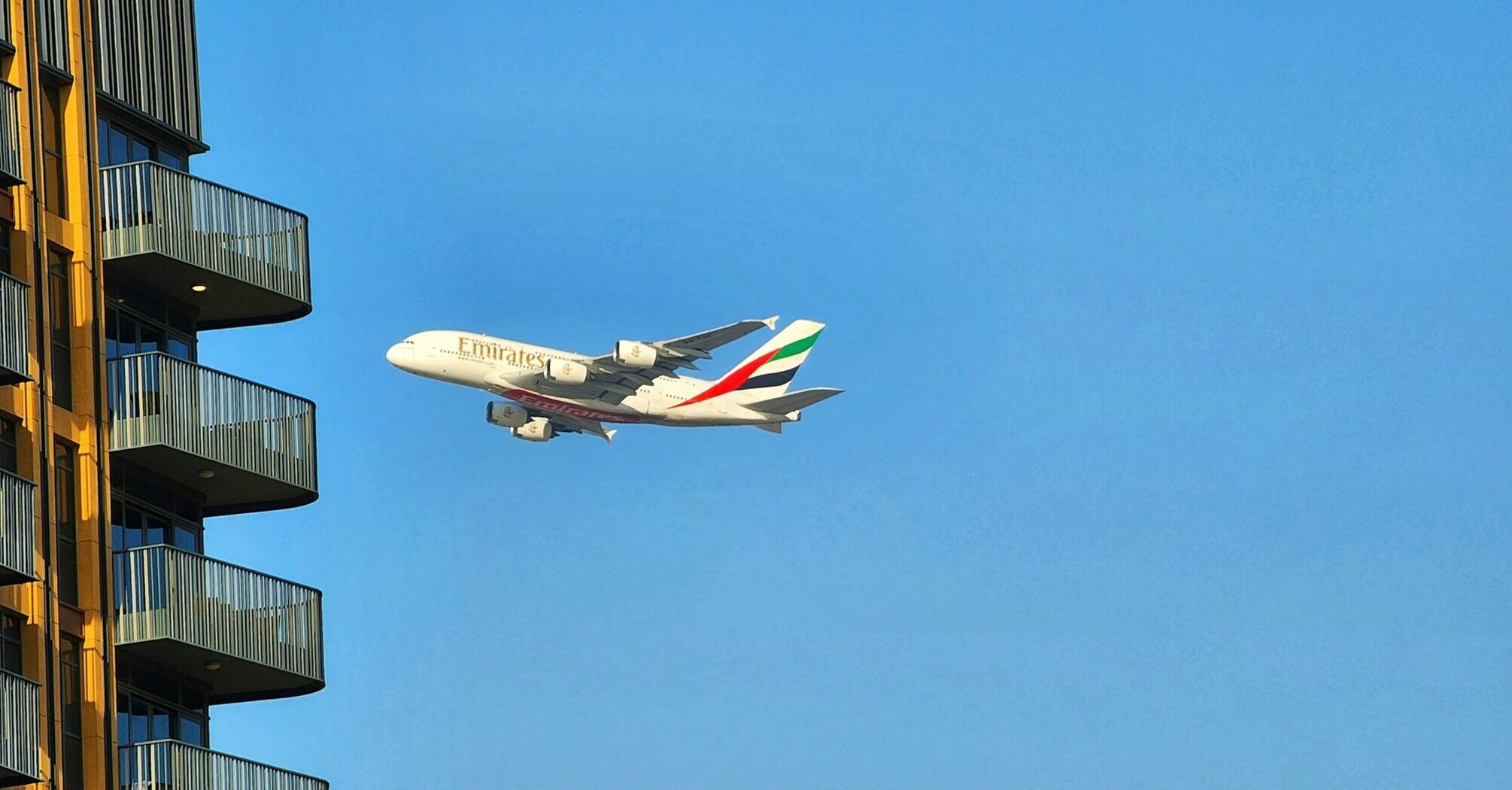 Emirates A380 flying close to a residential building under a clear blue sky