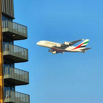 Emirates A380 flying close to a residential building under a clear blue sky