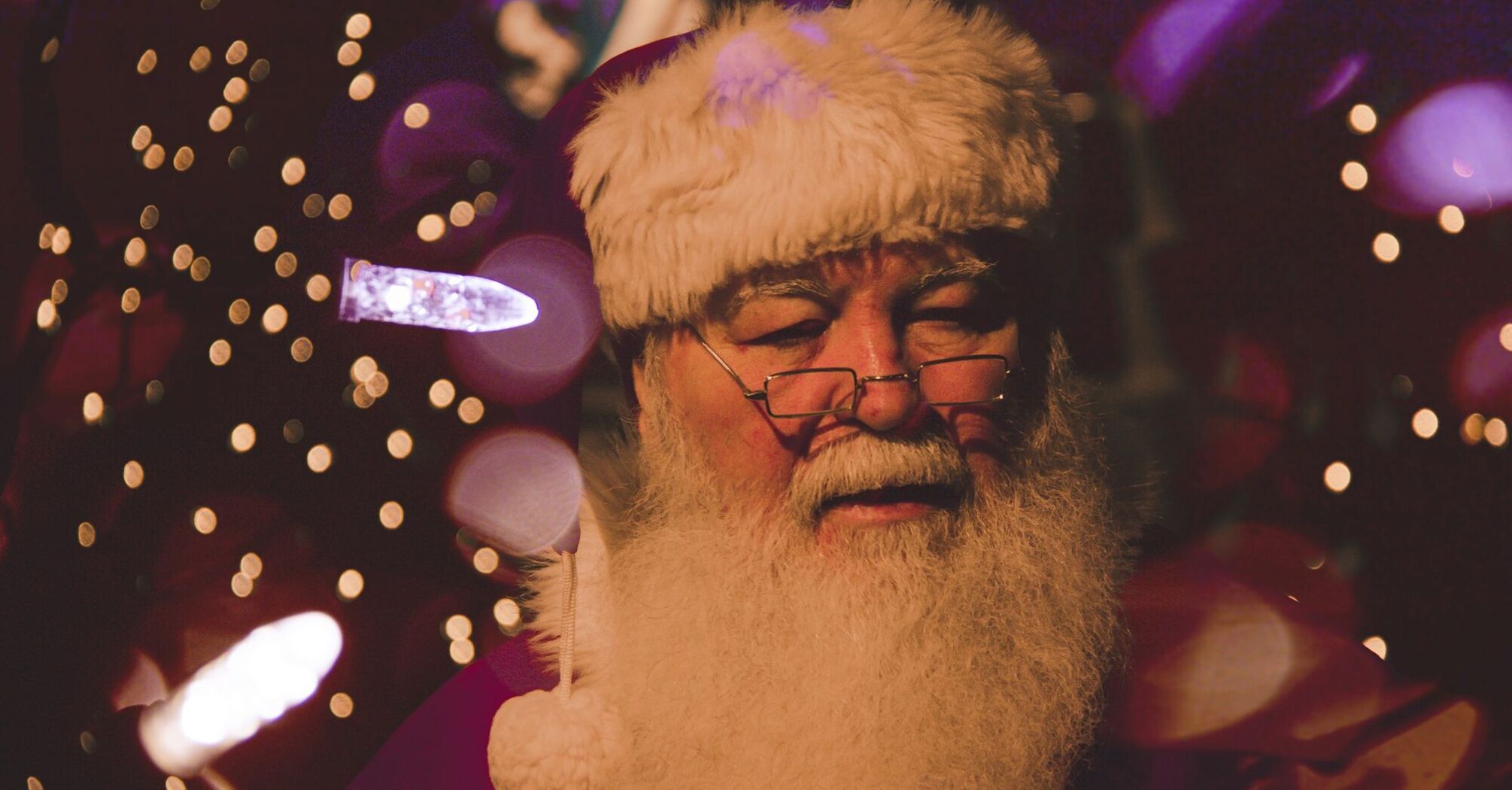 A close-up of Santa Claus with festive lights in the background, creating a warm and cheerful holiday atmosphere