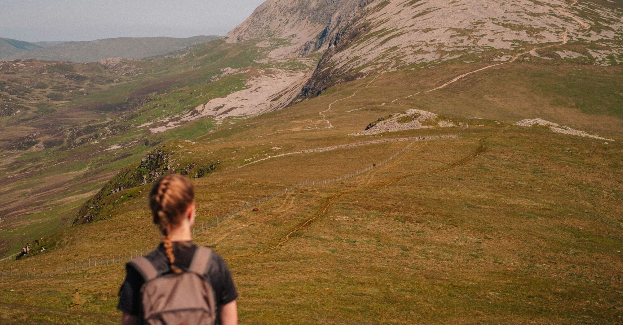 A hiker with a backpack walking through a scenic mountainous landscape under clear skies