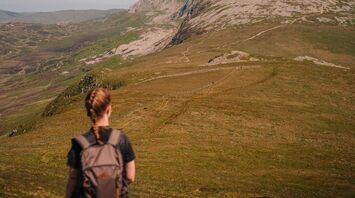 A hiker with a backpack walking through a scenic mountainous landscape under clear skies
