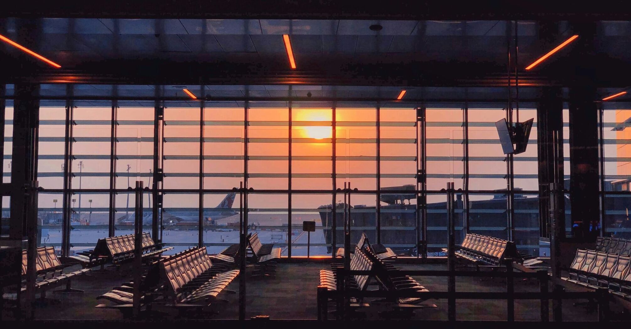 Hamad International Airport terminal at sunset with empty seats and a parked airplane in the background