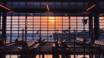 Hamad International Airport terminal at sunset with empty seats and a parked airplane in the background