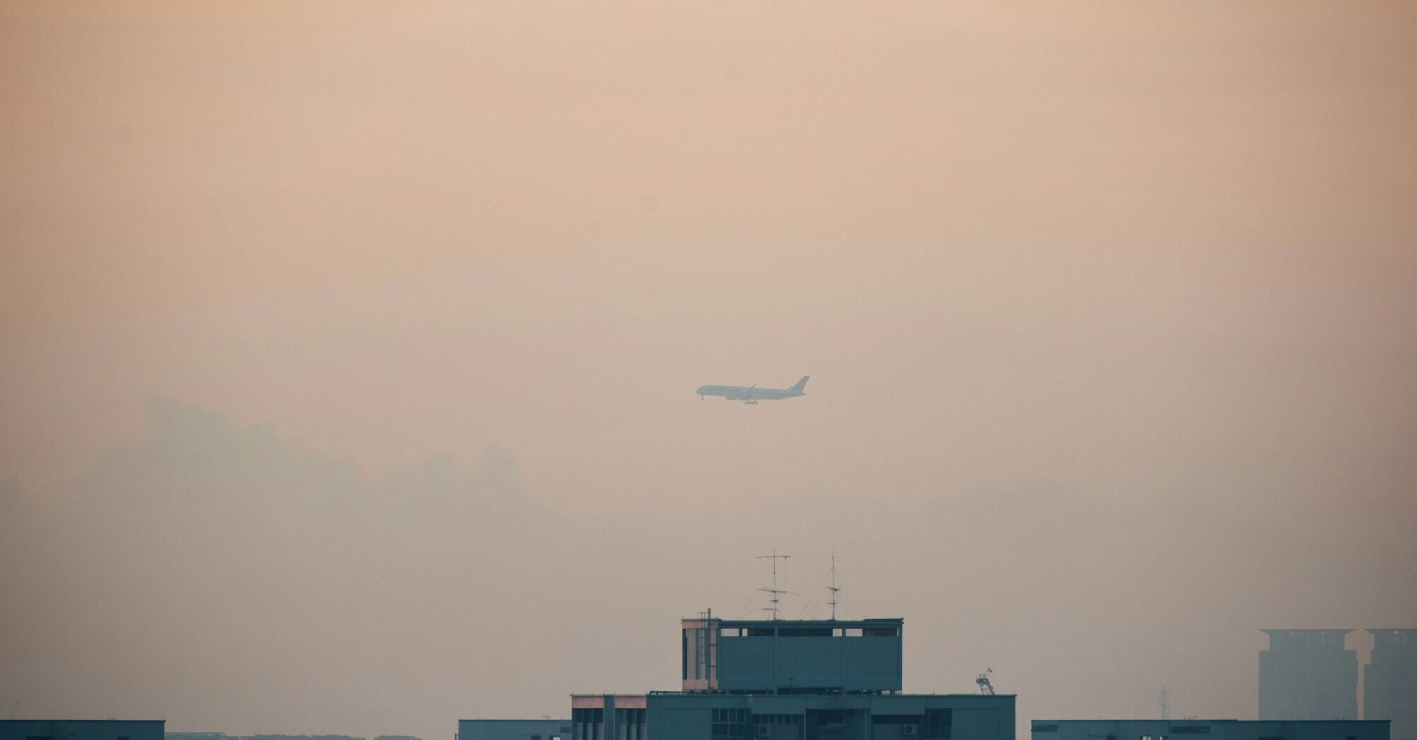 Airplane flying through dense fog over city buildings, with low visibility affecting the skyline