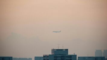 Airplane flying through dense fog over city buildings, with low visibility affecting the skyline