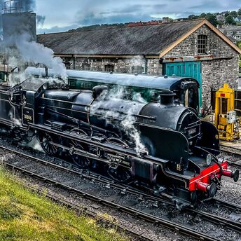 A historic Swanage Railway steam locomotive with passenger carriages near a vintage railway building