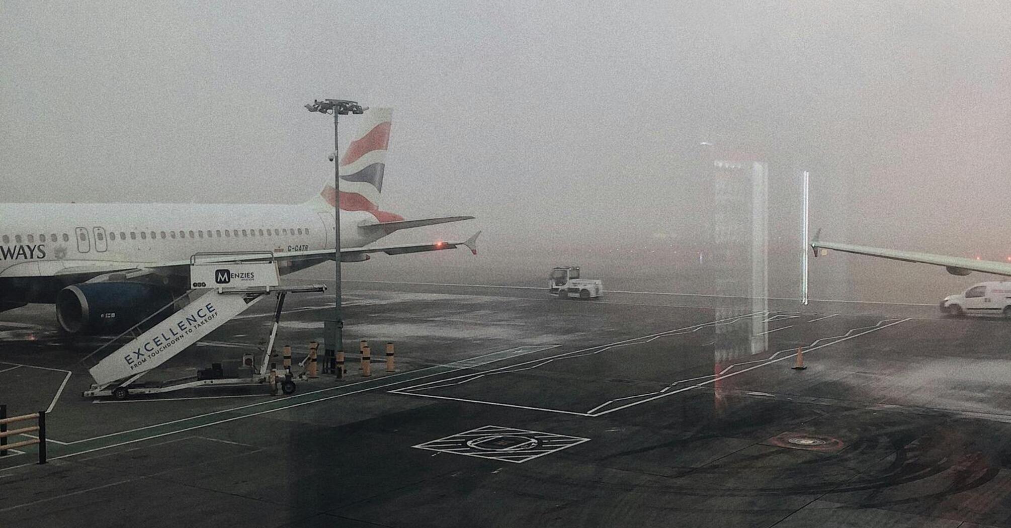 A foggy airport runway with a parked British Airways plane