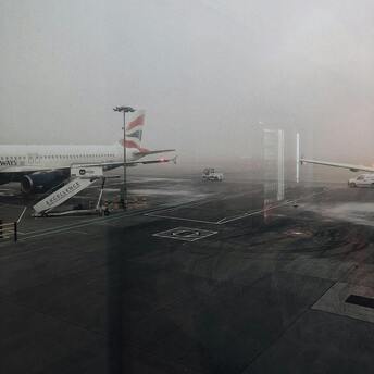 A foggy airport runway with a parked British Airways plane