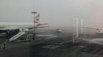 A foggy airport runway with a parked British Airways plane
