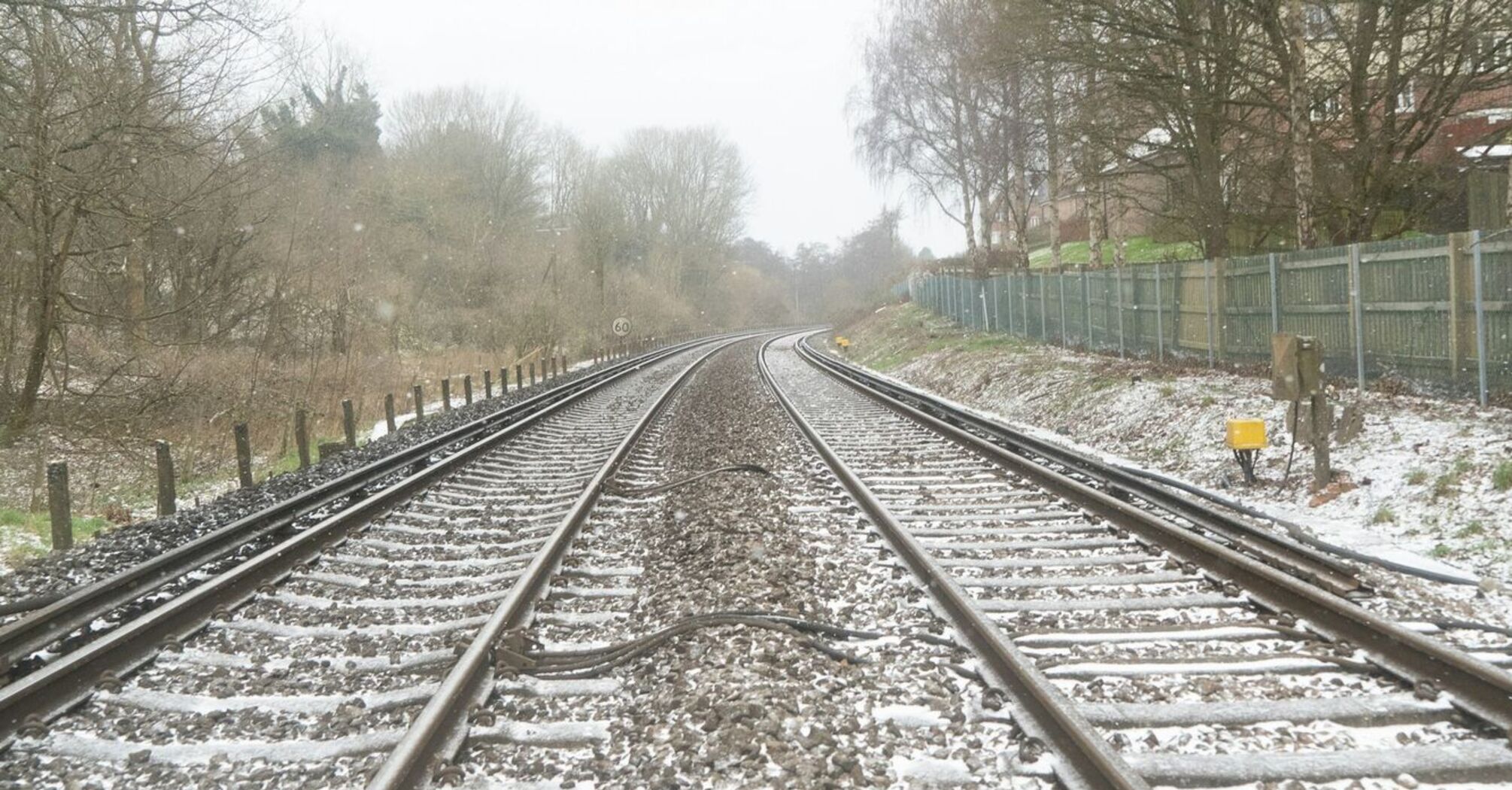 Snow-dusted railway tracks bordered by trees and fencing on a quiet winter day