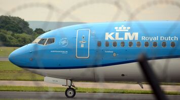 A KLM Royal Dutch Airlines plane taxiing on a runway with a blurred barbed wire fence in the foreground