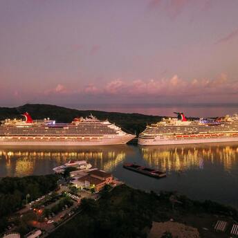 Two illuminated cruise ships docked at sunset