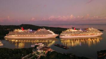 Two illuminated cruise ships docked at sunset