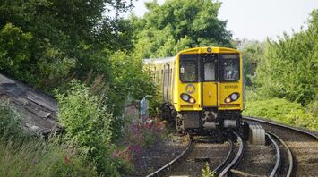 A yellow Merseyrail train traveling through a green countryside setting