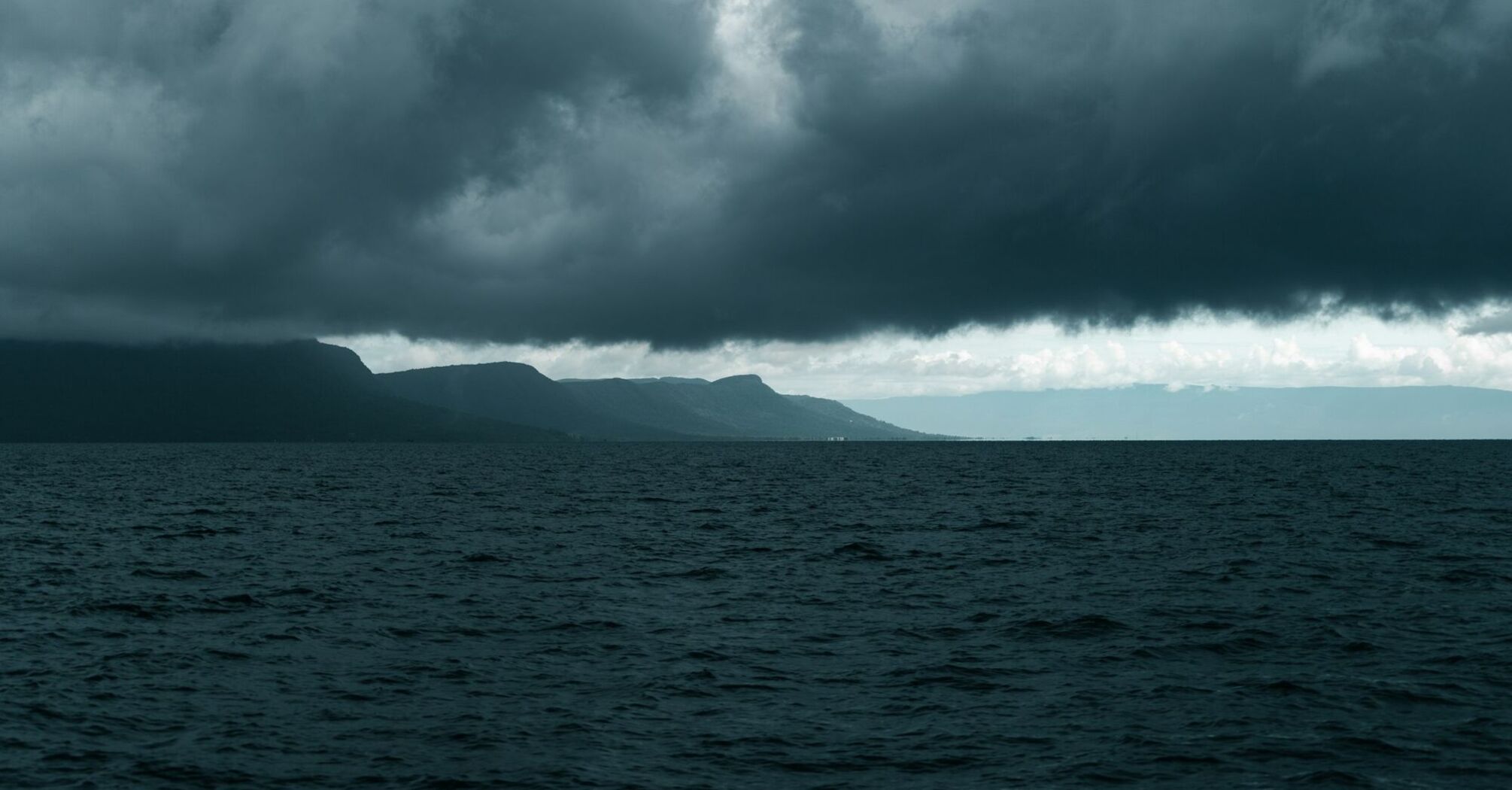 Dark storm clouds over the sea with a mountainous coastline in the background