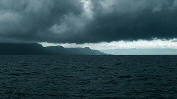 Dark storm clouds over the sea with a mountainous coastline in the background