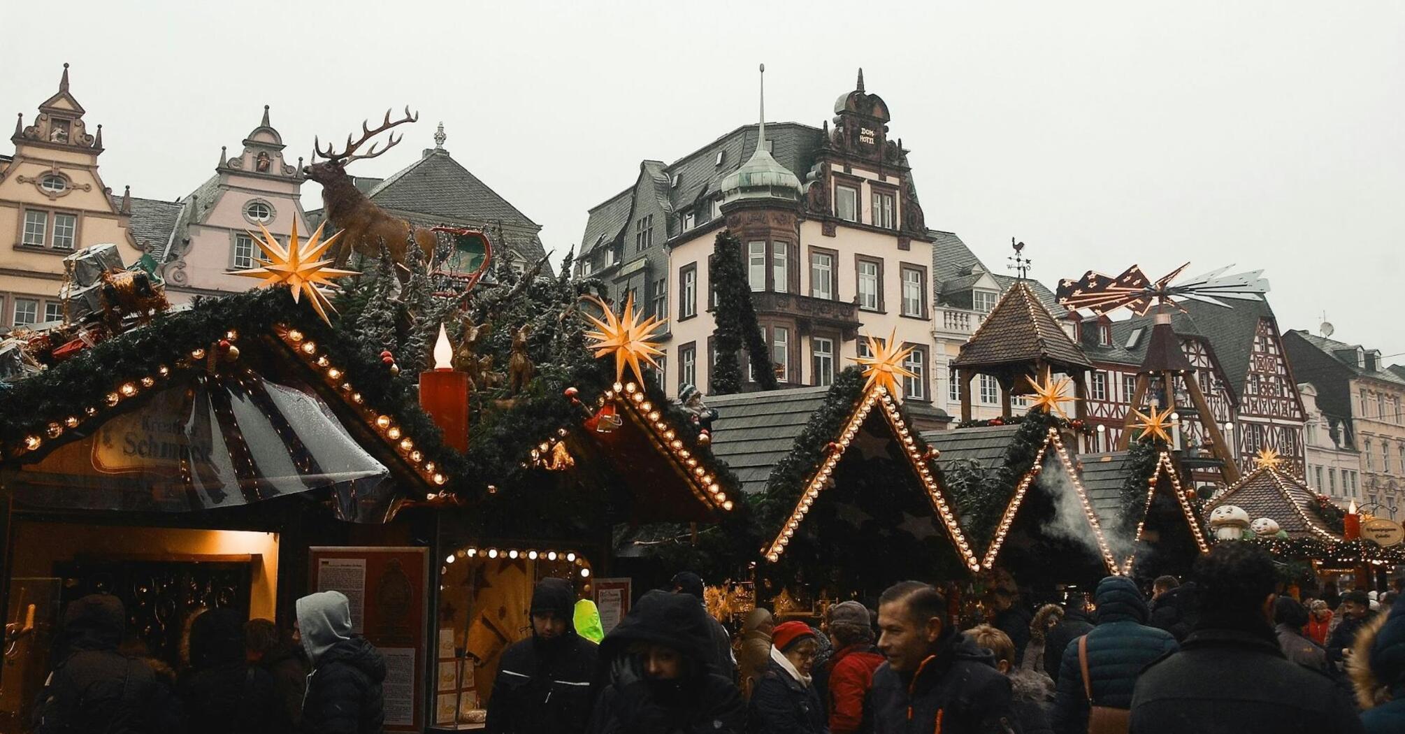 Christmas market stalls with festive decorations, lights, and a reindeer sculpture in a historic European town square