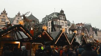 Christmas market stalls with festive decorations, lights, and a reindeer sculpture in a historic European town square