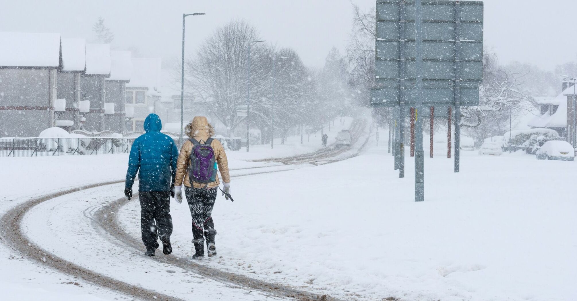 Two people walking through heavy snowfall on a residential street in Scotland