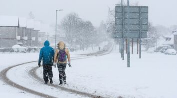 Two people walking through heavy snowfall on a residential street in Scotland