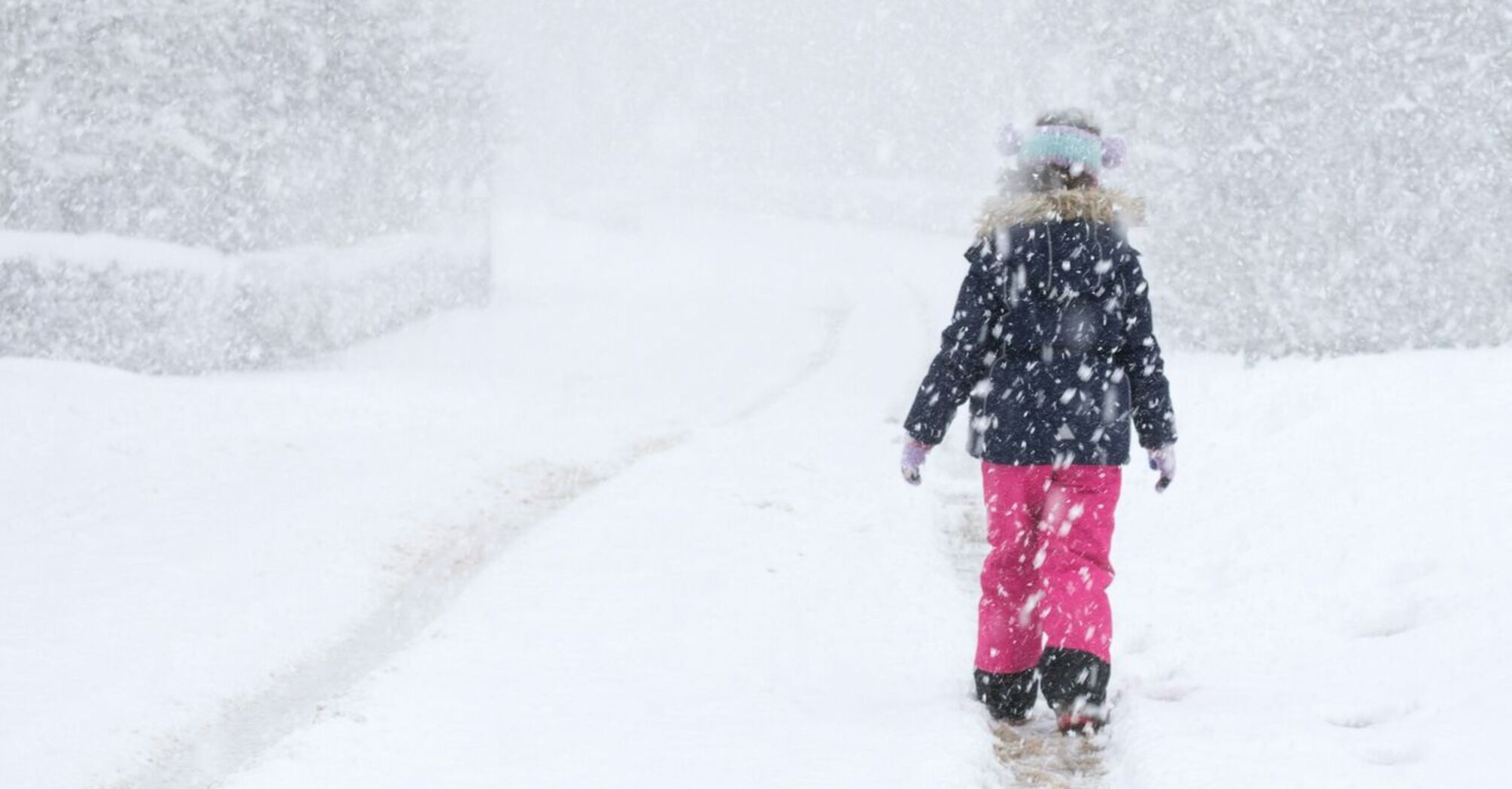 Person walking alone on a snow-covered path during heavy snowfall, surrounded by winter scenery