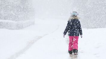 Person walking alone on a snow-covered path during heavy snowfall, surrounded by winter scenery