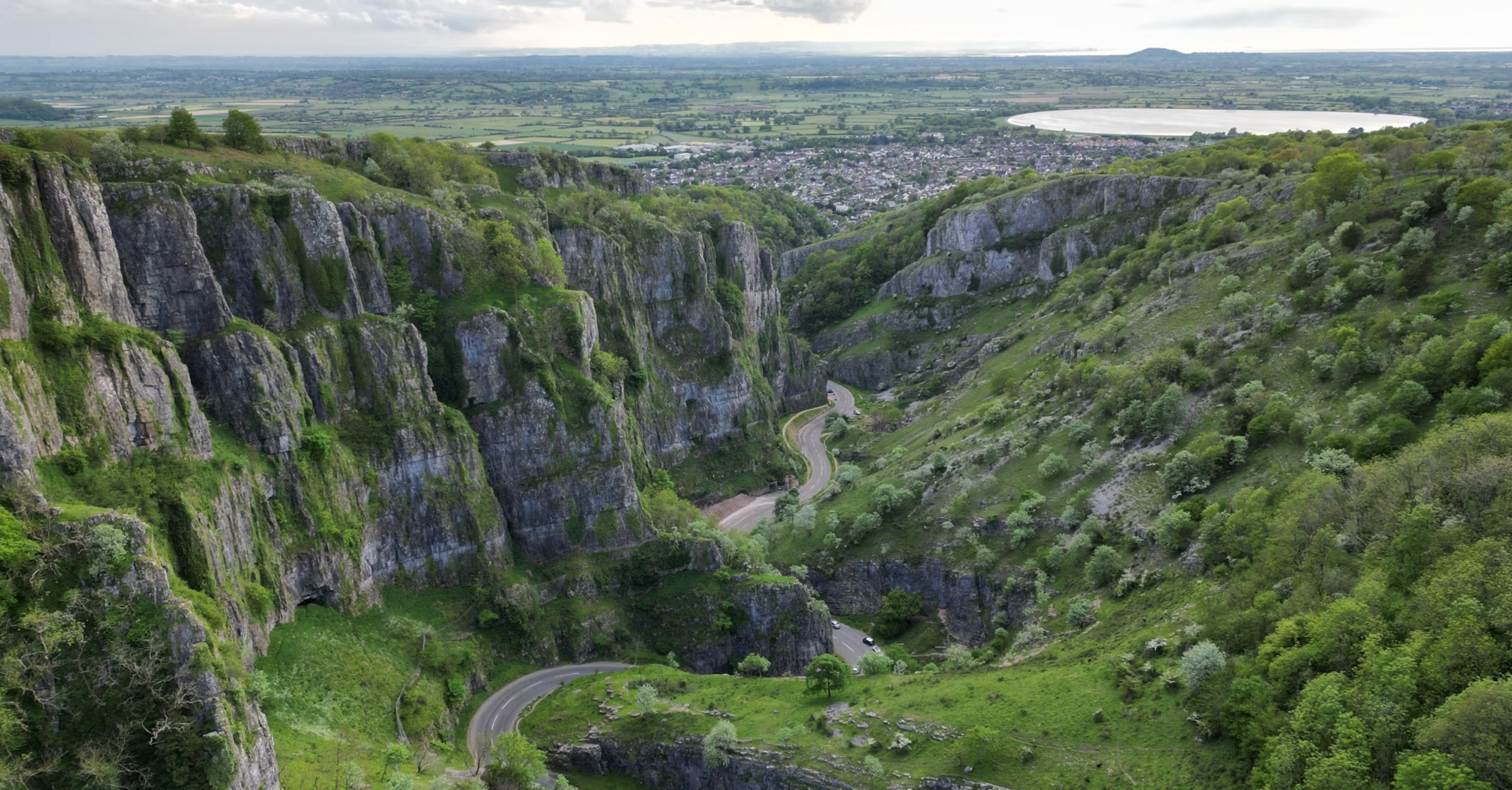 A view of Cheddar Gorge in Somerset, England, showcasing steep cliffs and winding roads surrounded by lush greenery