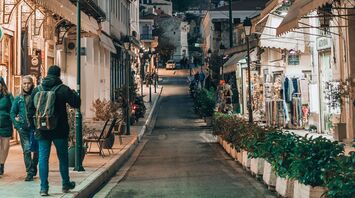 A picturesque street in Athens with a view of the Acropolis in the background, lined with local shops and evening lights