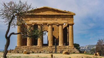 Ancient Greek temple with Doric columns surrounded by a blooming tree under a clear blue sky
