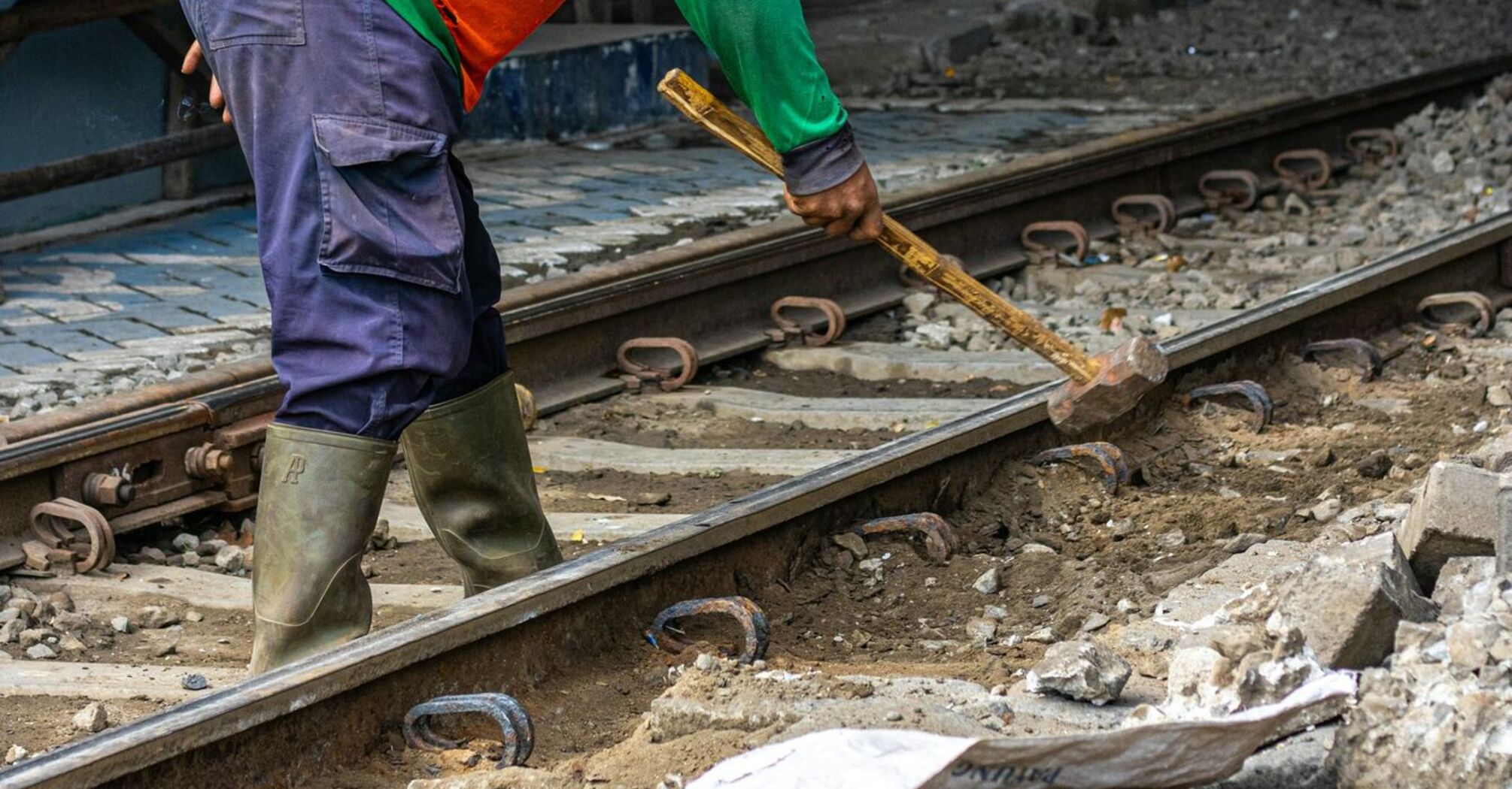 A railway worker in safety gear repairing tracks with a hammer