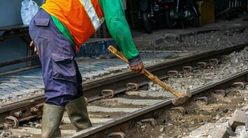 A railway worker in safety gear repairing tracks with a hammer