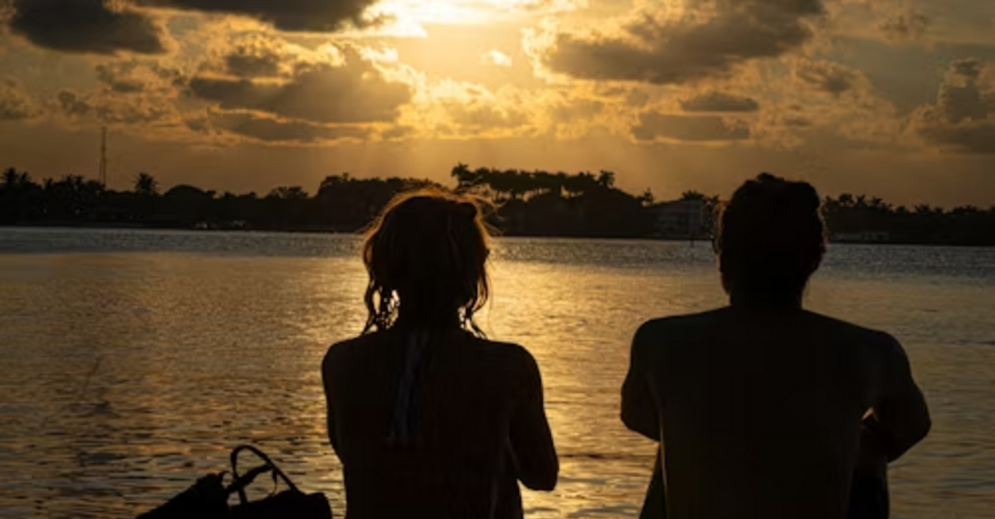 A couple sitting on the beach watching a sunset over the water, enjoying a peaceful moment together