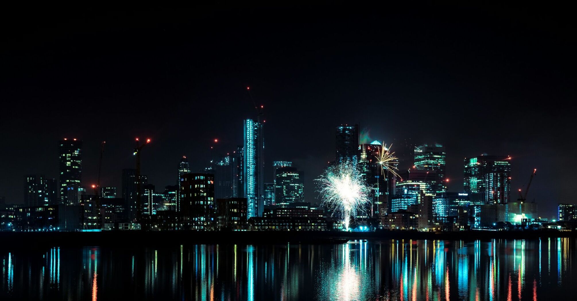 City skyline at night with fireworks and reflections on water