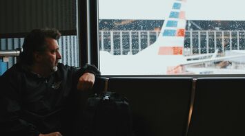 A man sitting by a window at an airport, looking out at a plane in rainy weather