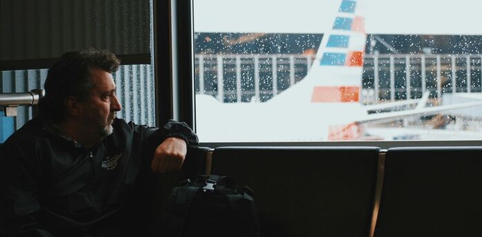 A man sitting by a window at an airport, looking out at a plane in rainy weather