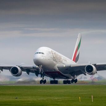 Emirates plane taking off from the runway under a cloudy sky near an airport terminal